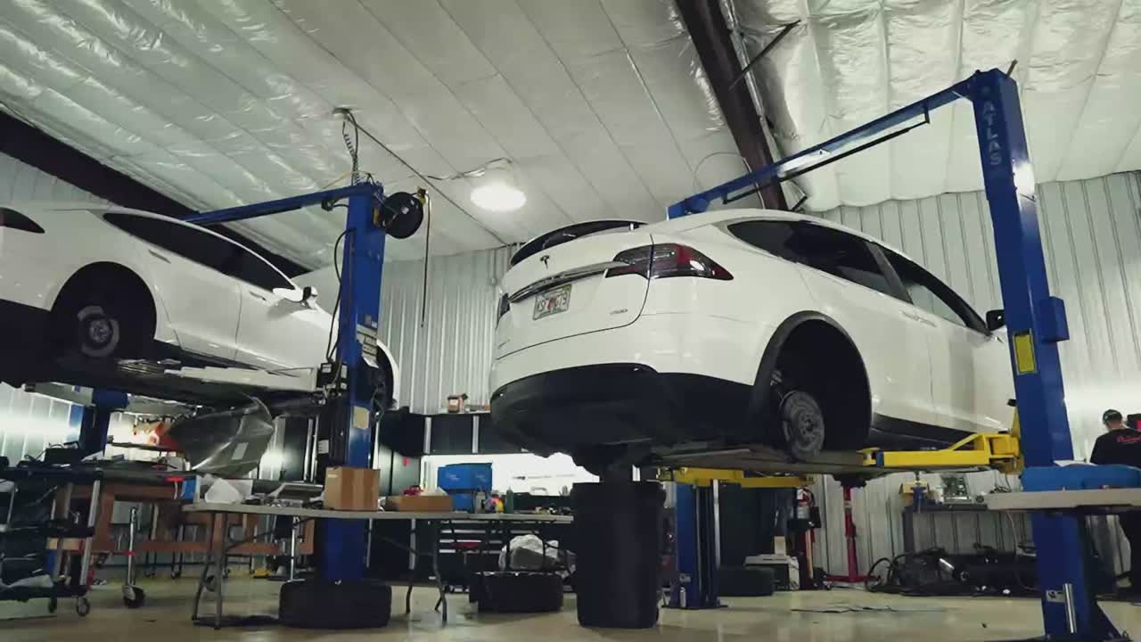 Two high-mileage electric vehicles raised on service lifts inside a repair garage